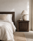 Bulu Bedside in Chocolate Elm styled beside a timber bed in a warm neutral bedroom with natural linen, soft sunlight and earthy textures.