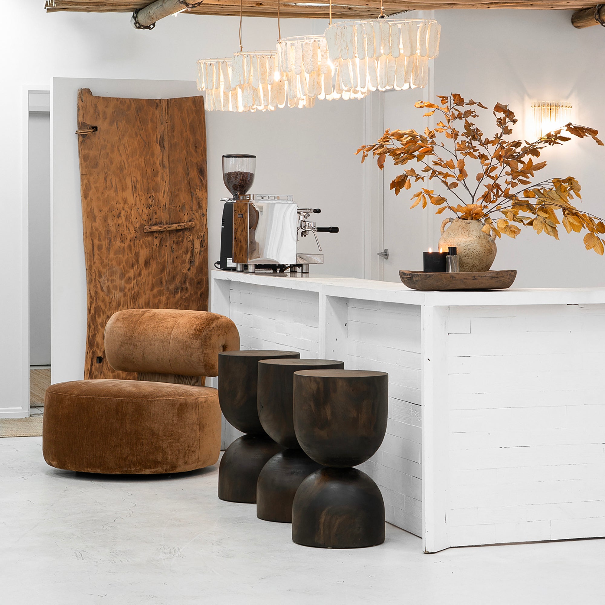 Contemporary café interior featuring Uniqwa Amma pendant lights, iggy velvet occasional chair, and trio of dark timber mele Stools at a white counter with autumnal styling