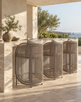 Cala Outdoor Barchair with curved woven detailing and neutral upholstery, styled along a stone bar in a coastal outdoor setting.