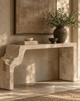 Uniqwa Collections Duna Console in Fossil Stone, featuring an asymmetrical sculptural form styled with decorative vessels, books and greenery in a warm, naturally lit interior.