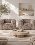 Pair of Harlow one seater sofas in Biscuit upholstered in plush faux fur, styled in a bright contemporary living room with a round stone coffee table and soft neutral décor.