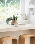 Uniqwa Collections Elula Counter Stools in natural oak featured in a contemporary white kitchen with curved travertine benchtop and rustic accents