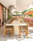 Mukalla dining table viewed from the front on a rooftop terrace with woven chairs soft neutral tones and sunlit outdoor dining ambience