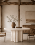 Oman dining table with a sculptural round form styled in a warm neutral dining room with timber chairs, natural textures and rustic architectural details.