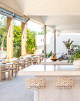 Salalah dining tables arranged beside a light filled rooftop bar with timber chairs soft stone finishes and greenery creating a relaxed open air dining atmosphere
