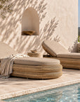 Satori Sun Lounger with woven curved base and neutral cushioning, styled in a warm poolside setting with natural stone and textured finishes.
