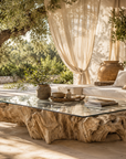 Outdoor setting with a natural wood coffee table, white cushions, and draped curtains.