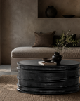Thembu coffee table in black with a sculptural layered silhouette styled in a moody contemporary living room with built in seating, earthy textures and natural accents.
