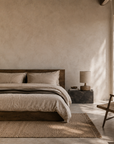 Zaya table lamp with a sculptural textured base and natural fabric shade styled on a dark stone bedside table in a warm minimalist bedroom with timber furnishings.