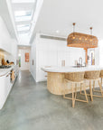 Uniqwa Collections Tula Bar Chairs featured in a modern coastal kitchen with white cabinetry, curved island bench, woven pendant lights, and polished concrete floors.