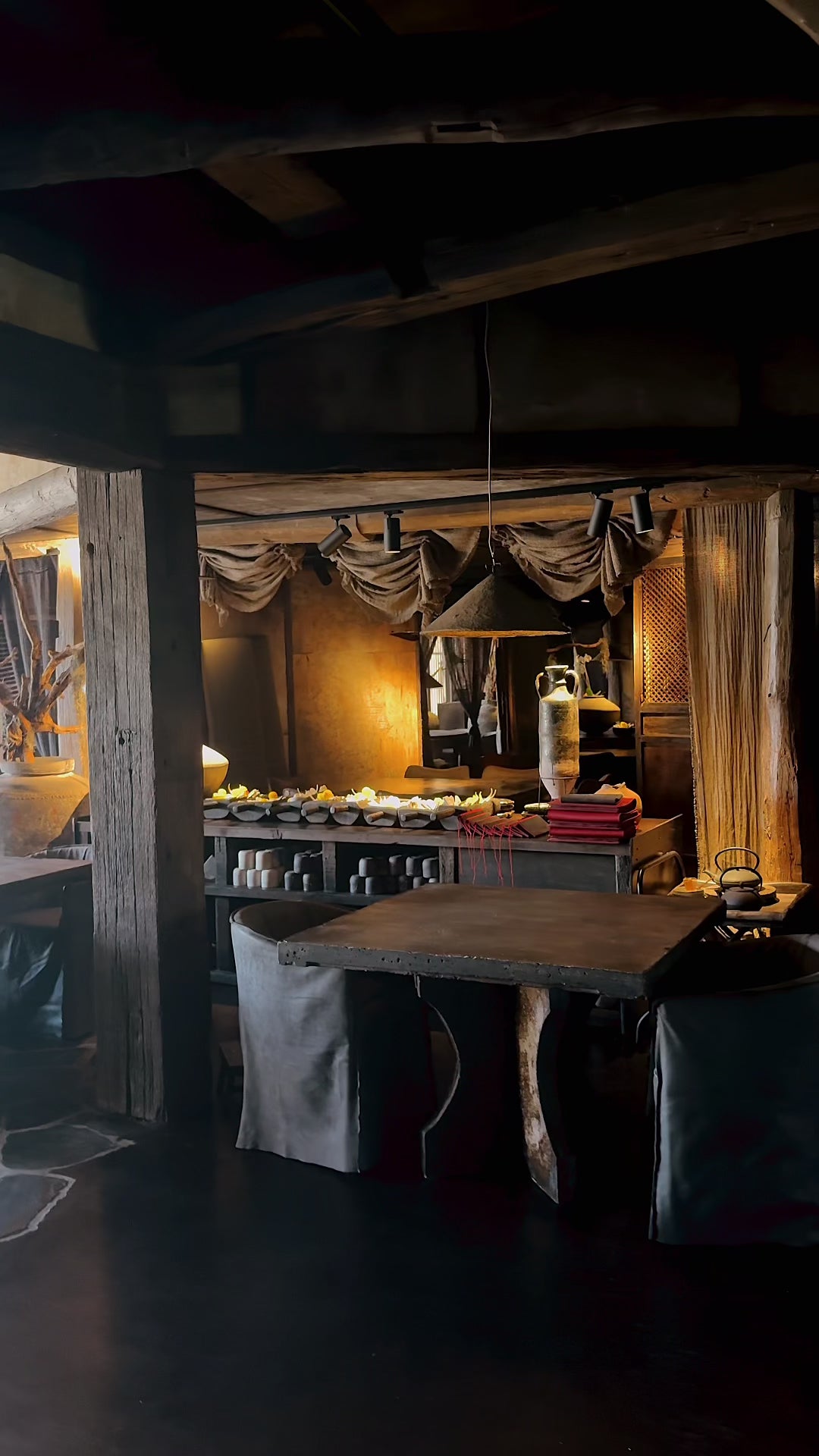 Hamilton dining chairs in African slate upholstery gathered around a textured round table beneath a Khufu pendant in dark roast, creating a moody layered interior with rich natural materials and soft ambient light.