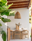 Outdoor dining setting featuring Uniqwa Collections teak chairs and travertine-look dining table beside a pool under a woven pendant light