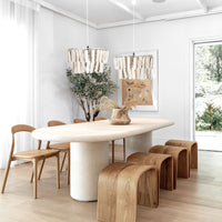 A contemporary dining space featuring a sculptural oval dining table, curved wooden stools, and minimalist wooden chairs, complemented by soft pendant lighting and organic décor