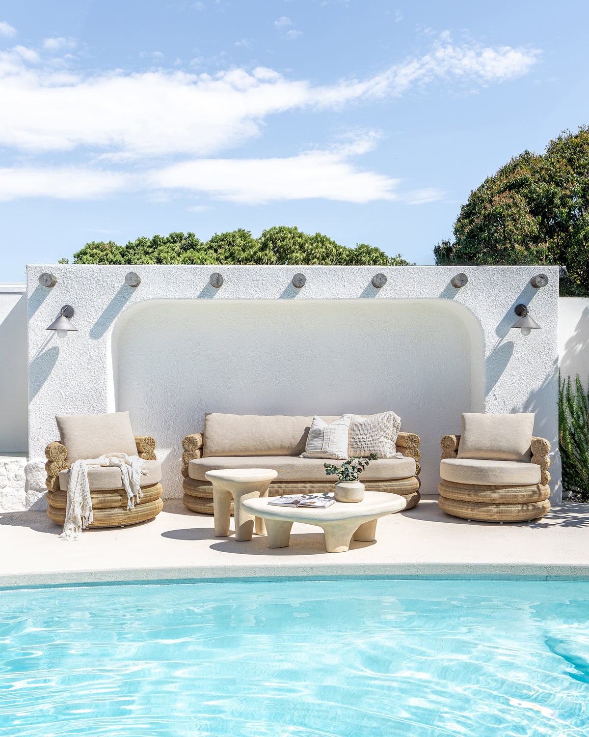 Bedu and Satori Collections styled together in a bright poolside setting with woven outdoor seating and sculptural tables.