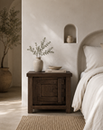 Bulu Bedside in Chocolate Elm styled beside a neutral bed in a Mediterranean inspired bedroom with warm natural textures and soft sunlight.