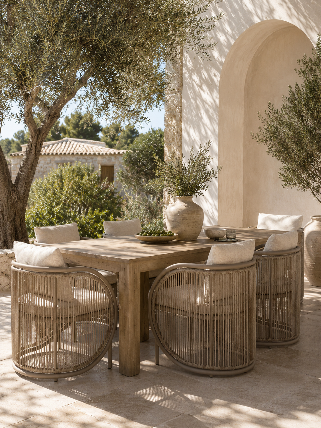Cala Dining Chair with a curved woven frame and neutral cushions, styled around a timber table in a Mediterranean-inspired outdoor dining setting