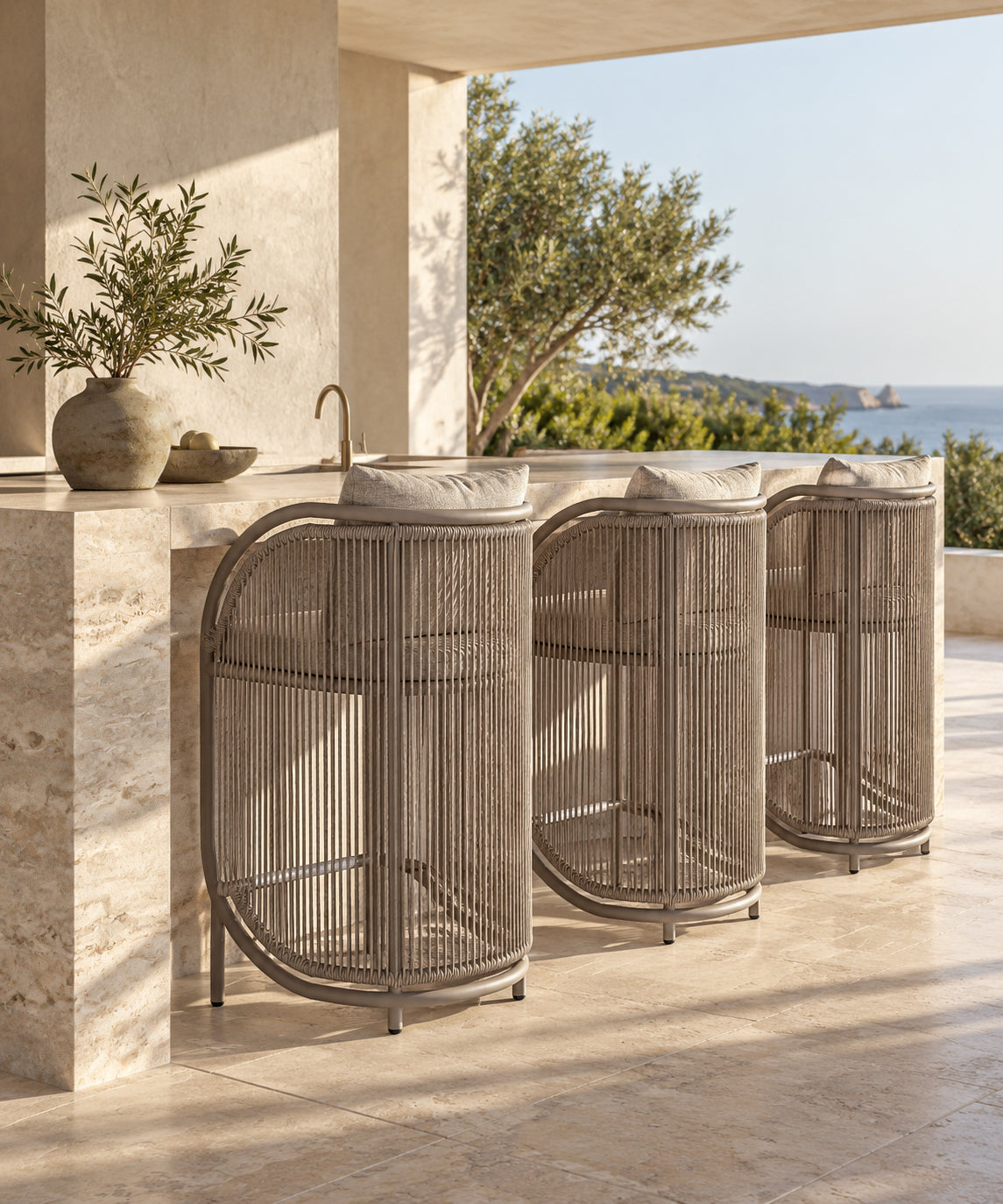 Cala Outdoor Barchair with curved woven detailing and neutral upholstery, styled along a stone bar in a coastal outdoor setting.