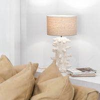 Uniqwa Collections Coral-inspired textured table lamp with a neutral fabric shade styled on a white console beside a tan leather lounge with layered cushions, creating a warm and organic living space