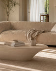 Davis Sofa with a curved upholstered form, styled in a warm living room beside a fireplace with a sculptural coffee table and soft linen curtains.