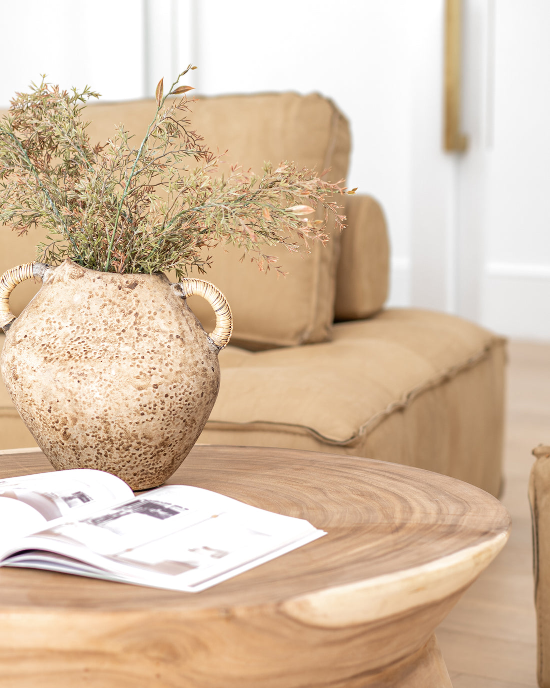 Vase with woven handles styled on a solid timber coffee table, paired with an open design book, set against a leather lounge in a warm and earthy-toned living space