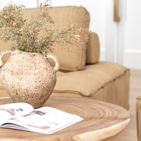 Vase with woven handles styled on a solid timber coffee table, paired with an open design book, set against a leather lounge in a warm and earthy-toned living space