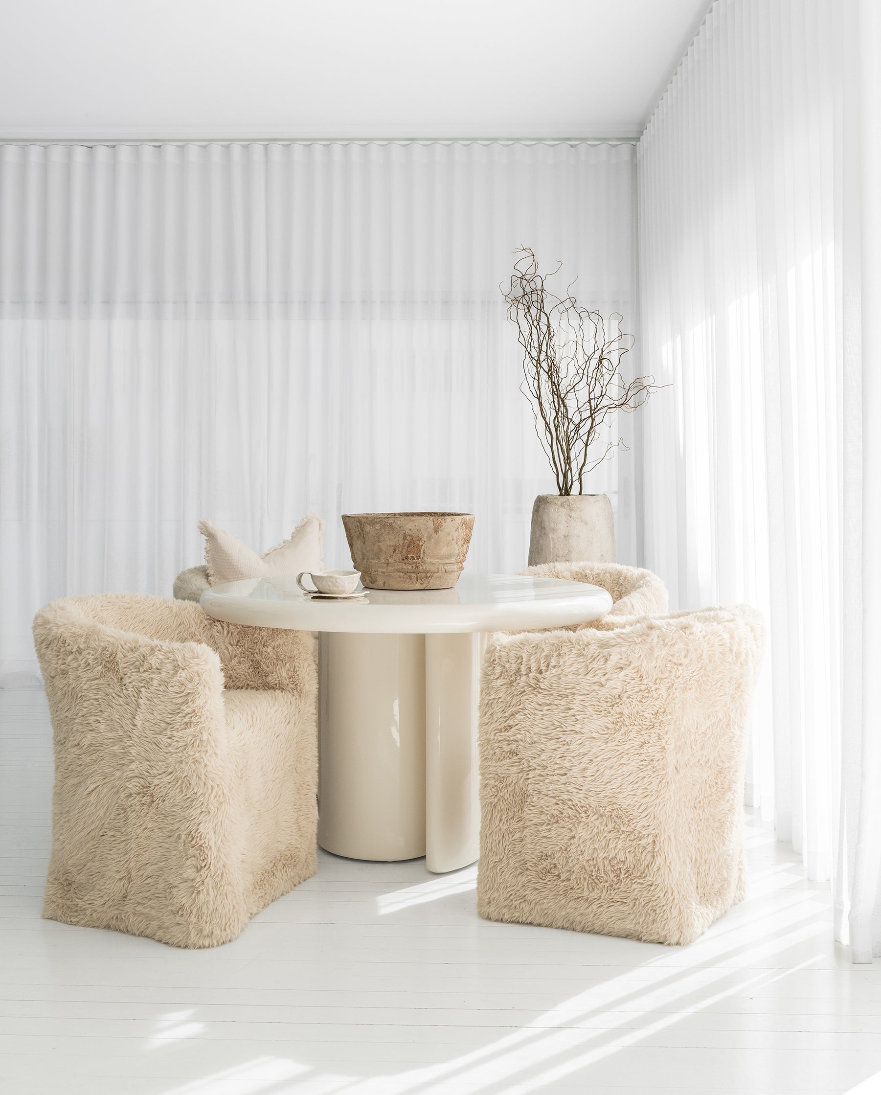Salalah Dining Table in High Gloss Vanilla with Hamilton Dining Chairs in Fur Luxe, styled with the Nusa Palm Planter and Bloom Mug