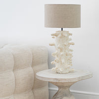 A beautifully handcrafted wooden side table paired with an organic sculptural lamp, featuring a textured natural finish. Styled next to a plush linen sofa, this setup exudes earthy sophistication and timeless elegance