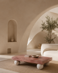 Jewel coffee table with a warm stone top and sculptural travertine sphere legs styled in a serene Mediterranean inspired living room with a curved sofa and arched architecture.
