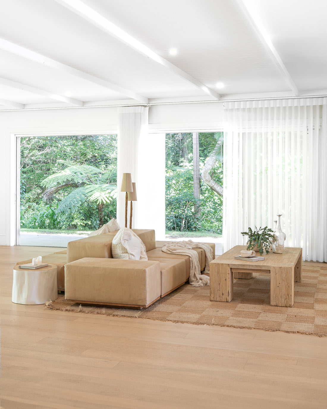 Leather modular sofa styled with textured cushions and a linen throw, paired with a reclaimed wood coffee table on a woven jute rug, creating a serene and organic living space with floor-to-ceiling views of lush greenery