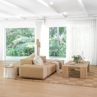 Leather modular sofa styled with textured cushions and a linen throw, paired with a reclaimed wood coffee table on a woven jute rug, creating a serene and organic living space with floor-to-ceiling views of lush greenery