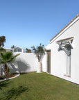Eucalyptus latte poles forming a natural timber shade above an arched window on a white coastal home.