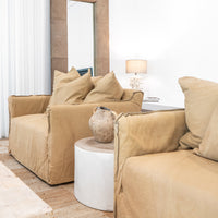 Leather sofa with oversized cushions styled with a vase on a round trunk side table, complemented by a textured rug and a coral-inspired table lamp in a refined organic living space