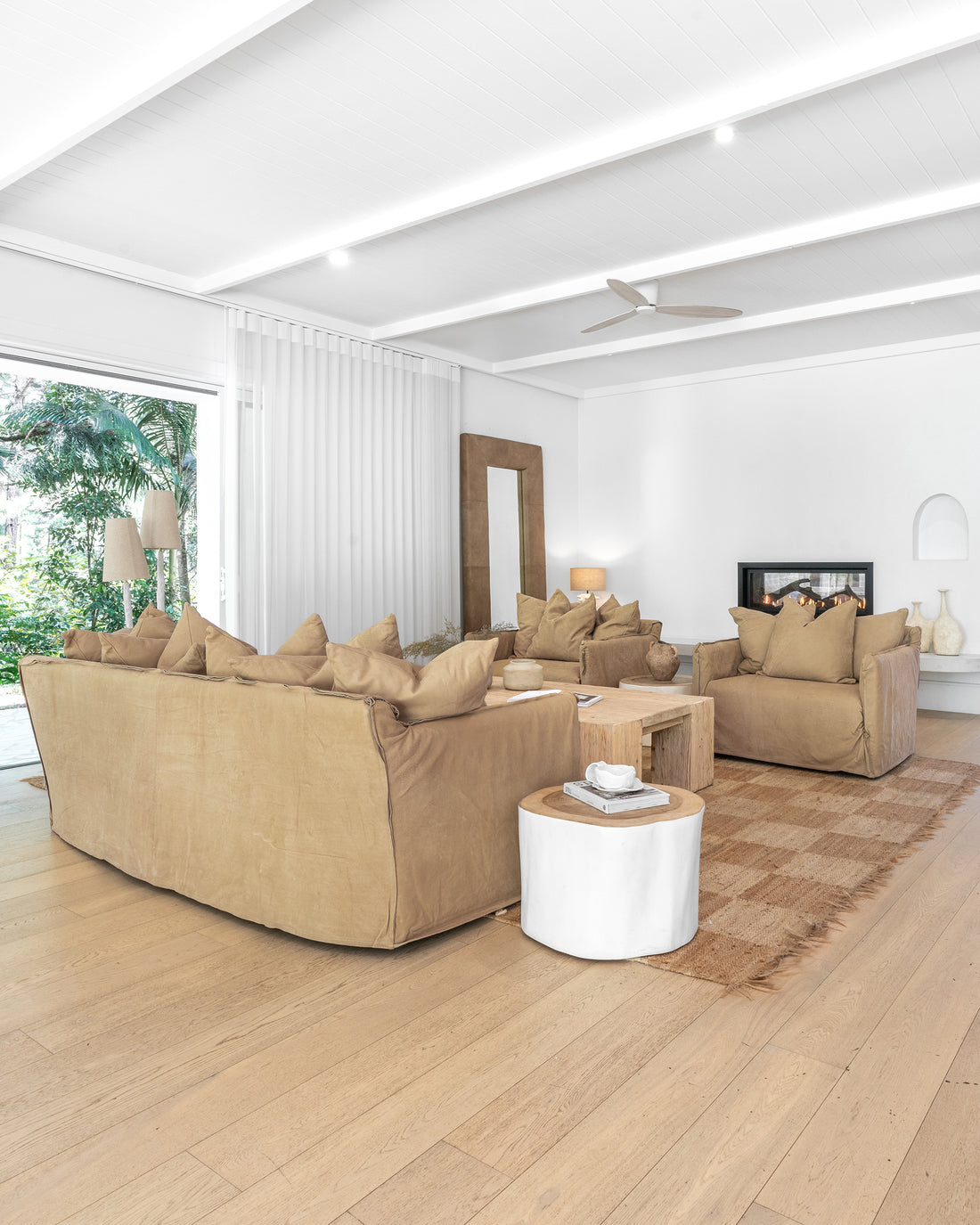 Leather sofa and armchairs styled with a reclaimed wood coffee table and textured cushions, complemented by a woven jute rug, sculptural side table, and a fireplace in a modern organic living room