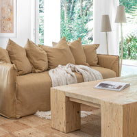 Leather sofa styled with oversized cushions and a textured throw, paired with a reclaimed wood coffee table on a woven jute rug, complemented by sculptural floor lamps in a serene organic living room