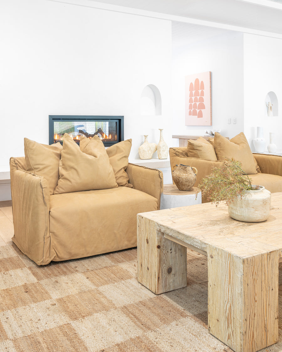 Leather sofa with oversized cushions styled around a reclaimed wood coffee table, complemented by a textured woven rug, ceramic vases, and a modern fireplace in a warm, organic living space