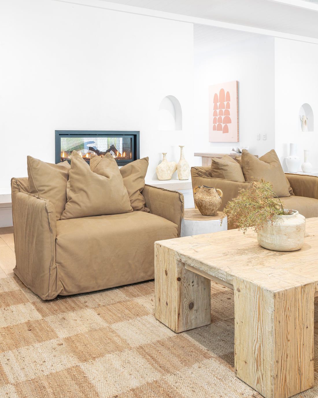 Leather sofa with oversized cushions styled around a reclaimed wood coffee table, complemented by a textured woven rug, ceramic vases, and a modern fireplace in a warm, organic living space