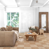 Modern living room featuring a leather sofa, handcrafted timber coffee table, and woven jute rug, complemented by a leather-framed mirror and minimalist decor in a serene, natural setting