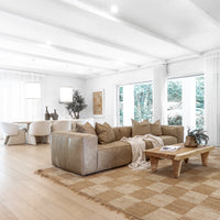 Leather sofa styled with textured cushions and a linen throw, paired with a reclaimed wood coffee table on a woven jute rug, seamlessly flowing into a modern dining area with plush boucle chairs and pendant lighting