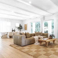 Leather sofa styled with textured cushions and a linen throw, paired with a reclaimed wood coffee table on a woven jute rug, seamlessly flowing into a modern dining area with plush boucle chairs and pendant lighting