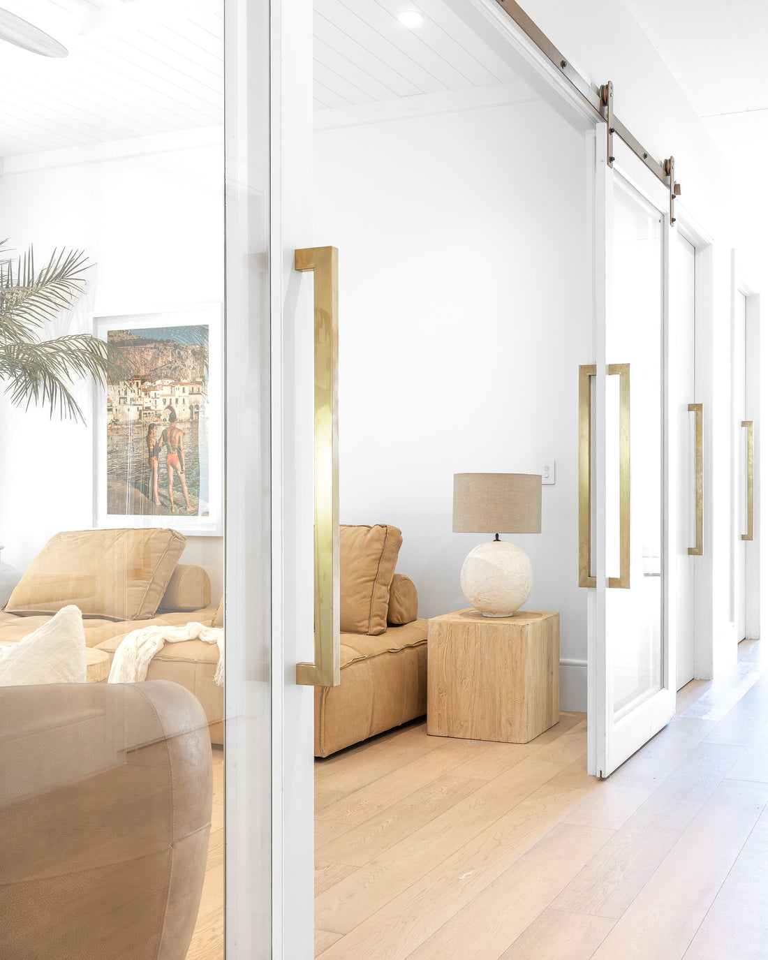 Leather lounge styled with a timber side table and a textured table lamp, framed by glass sliding doors with brass handles, creating a seamless connection between spaces in a modern organic living area