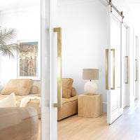 Leather lounge styled with a timber side table and a textured table lamp, framed by glass sliding doors with brass handles, creating a seamless connection between spaces in a modern organic living area