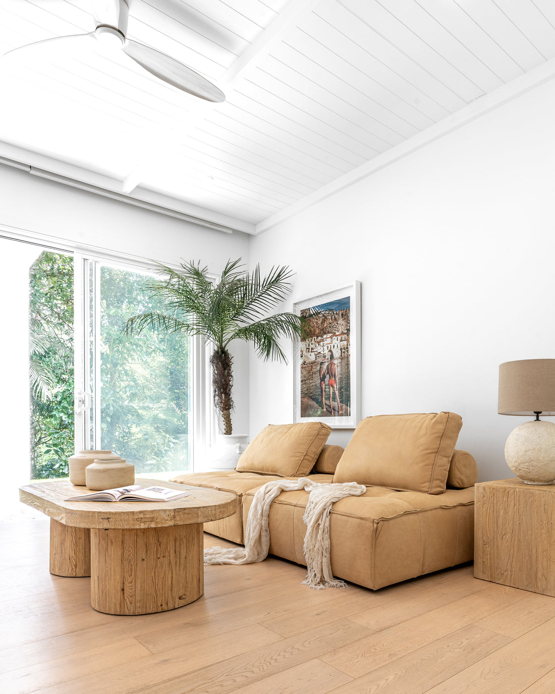 Leather modular sofa styled with a reclaimed wood coffee table, textured linen throws, and ceramic vases, complemented by a neutral-toned table lamp and lush greenery in a bright, organic living space