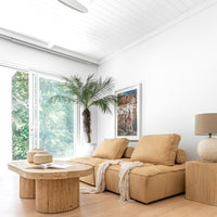 Leather modular sofa styled with a reclaimed wood coffee table, textured linen throws, and ceramic vases, complemented by a neutral-toned table lamp and lush greenery in a bright, organic living space