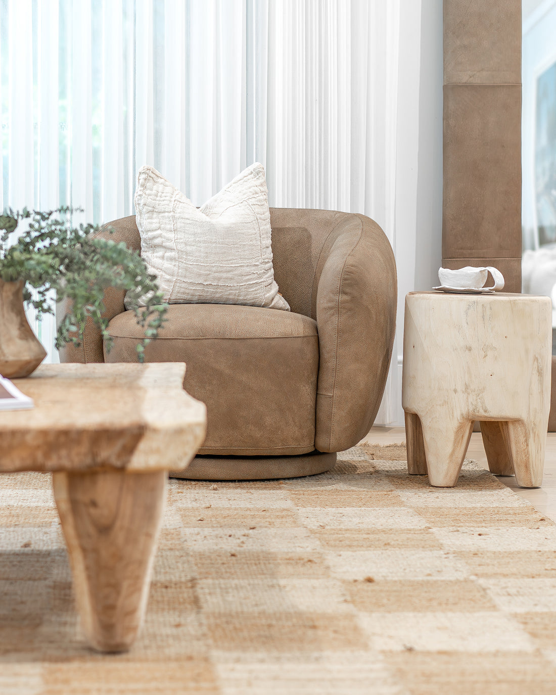 Uniqwa Collections leather swivel chair styled with a textured linen cushion, paired with a handcrafted coffee table and a raw timber side table on a natural woven rug, creating a warm and inviting living space