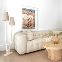 Fabric tufted sofa styled with a reclaimed wood coffee table and sculptural floor lamps, complemented by organic textures and a coastal-inspired framed artwork in a serene modern living space