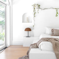 Minimalist bedroom featuring a white plaster built-in bed with soft earthy-toned bedding, complemented by the Sahra Table Lamp and cascading greenery for a serene and organic aesthetic