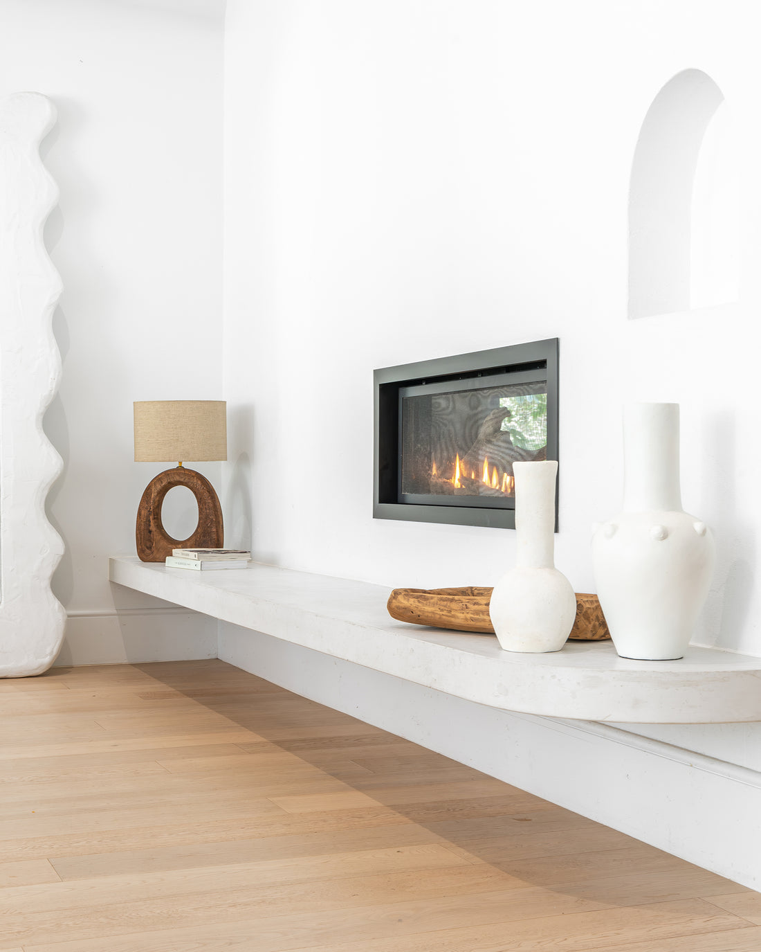 Uniqwa Collections a minimalist modern fireplace styled with sculptural ceramic vases, a rustic wooden bowl, and a contemporary table lamp, creating a warm and inviting atmosphere with organic textures and neutral tones