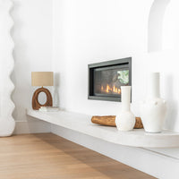 Uniqwa Collections a minimalist modern fireplace styled with sculptural ceramic vases, a rustic wooden bowl, and a contemporary table lamp, creating a warm and inviting atmosphere with organic textures and neutral tones