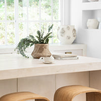 Minimalist kitchen space featuring sculptural wooden bar stools, a natural stone countertop, and earthy decor with organic ceramic vases and fresh greenery, creating a serene and inviting atmosphere