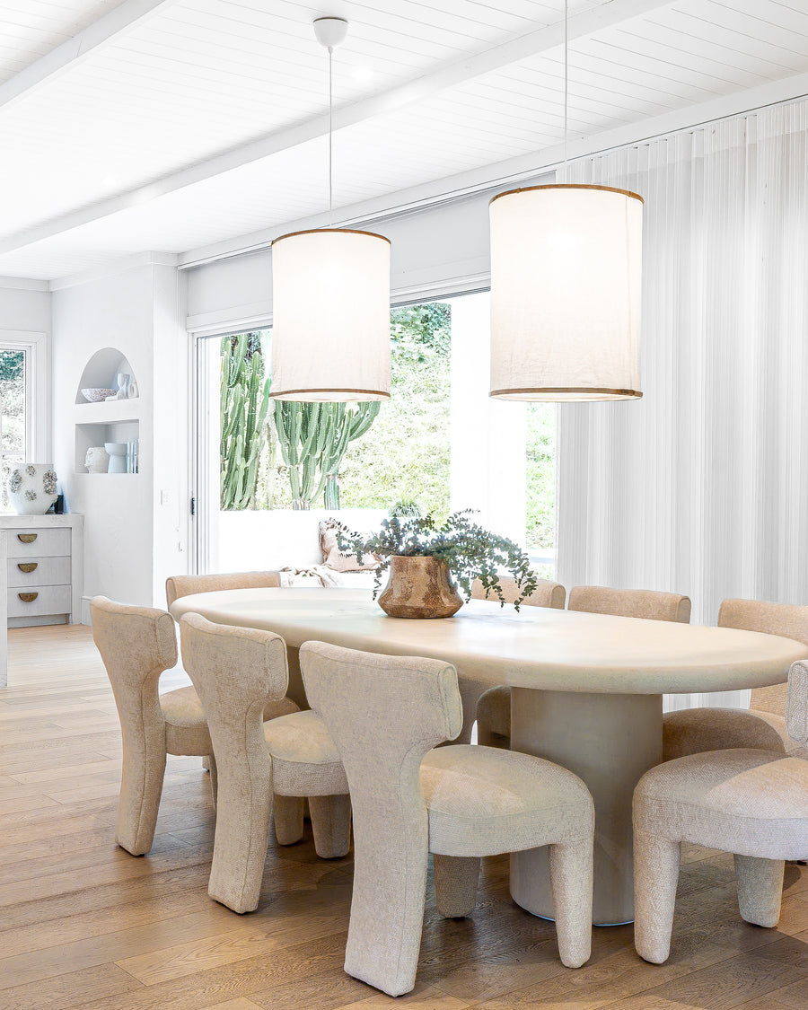 Stone dining table paired with sculptural boucle dining chairs, illuminated by oversized linen pendant lights, creating an inviting and textural modern dining space with natural light and organic decor.